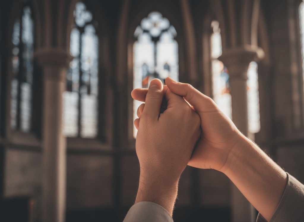 Two hands gently clasped in a gesture of solidarity and care, warm soft light, subtle church architecture blurred in background, minimalist and dignified, photographic style